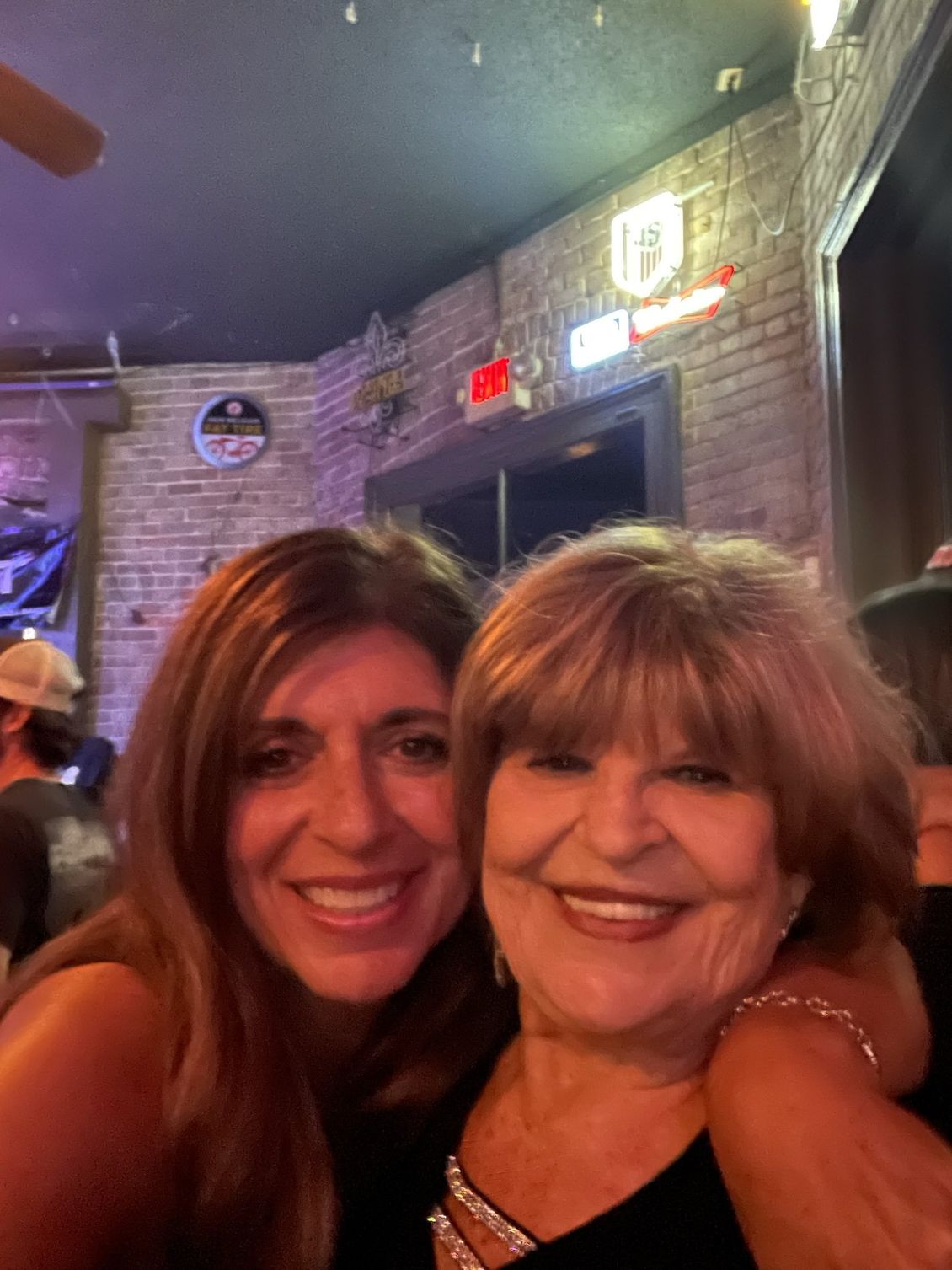 Two women smiling at the camera, close together. They are inside a bar with brick walls.