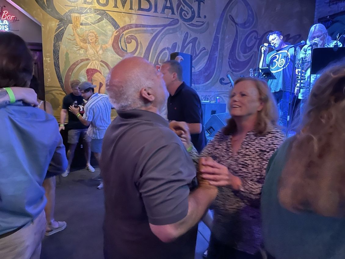 People dancing in a bar, band playing in the background. Wall mural reads 