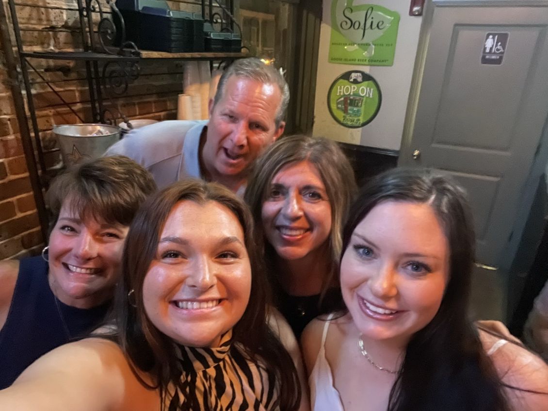 Group of people smiling, taking a selfie in a dimly lit bar.