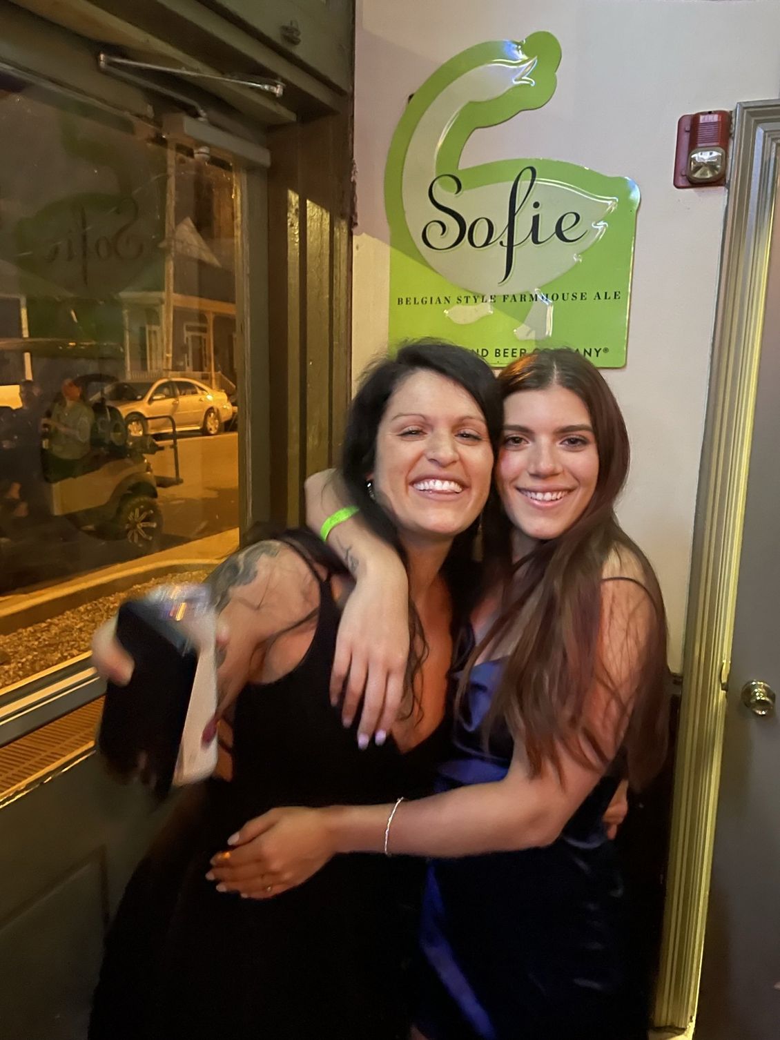 Two smiling women hugging in front of a sign that says 