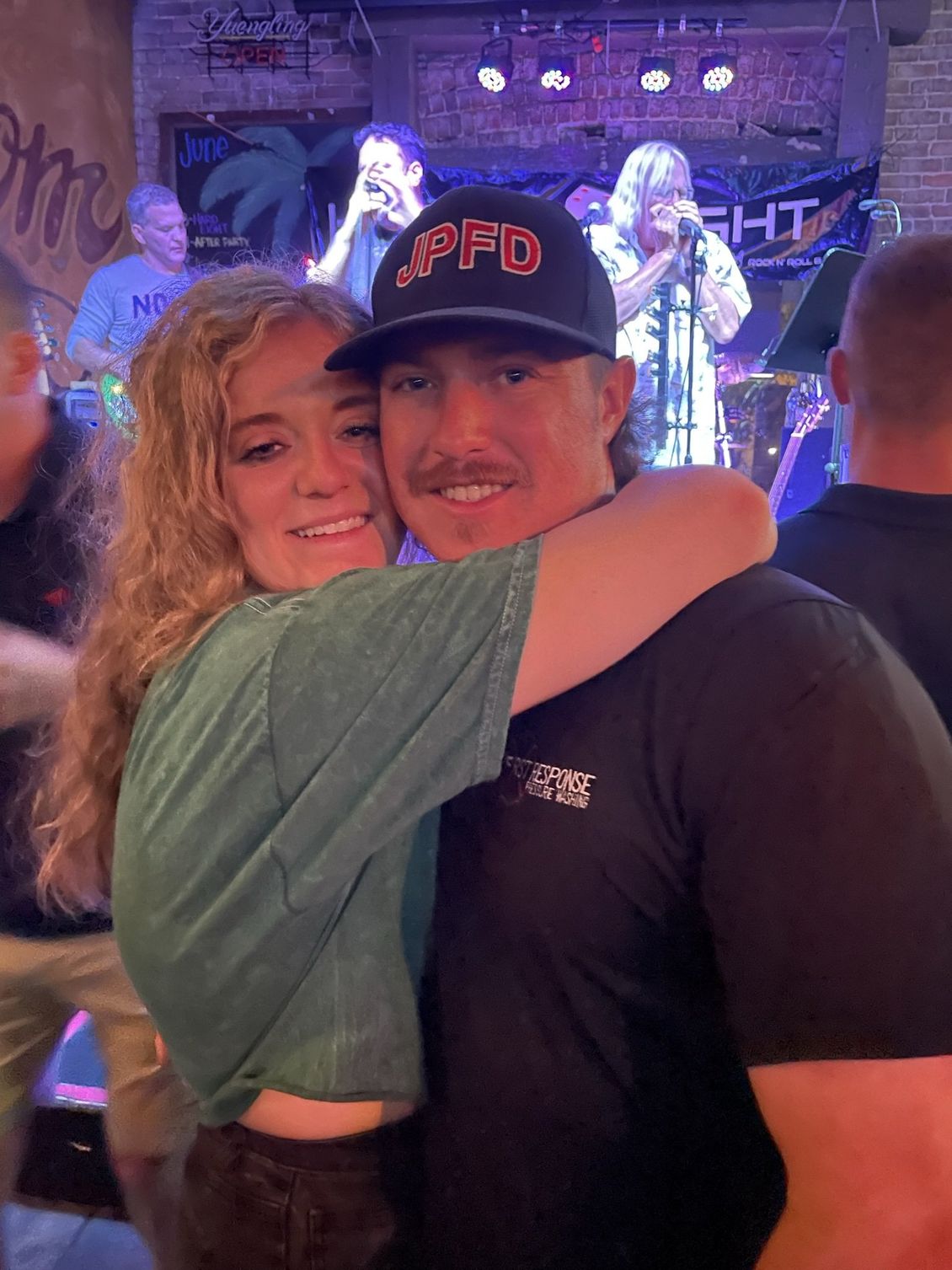 Woman hugs man wearing a hat that says 