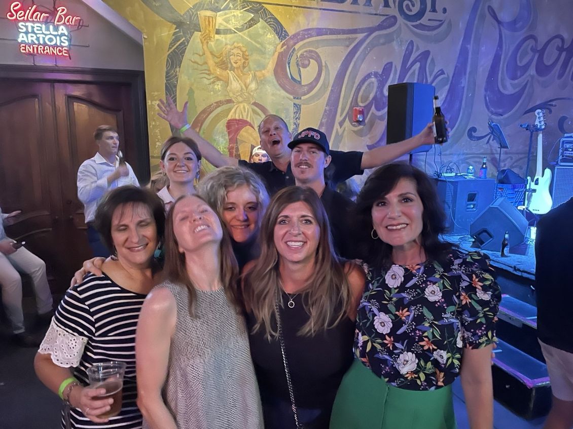 Group of people smiling and posing for a photo inside a bar with a mural.
