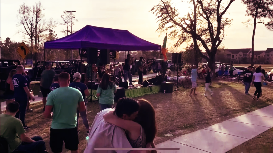 People gathered outdoors under a purple tent, hugging, and dancing at a daytime event.