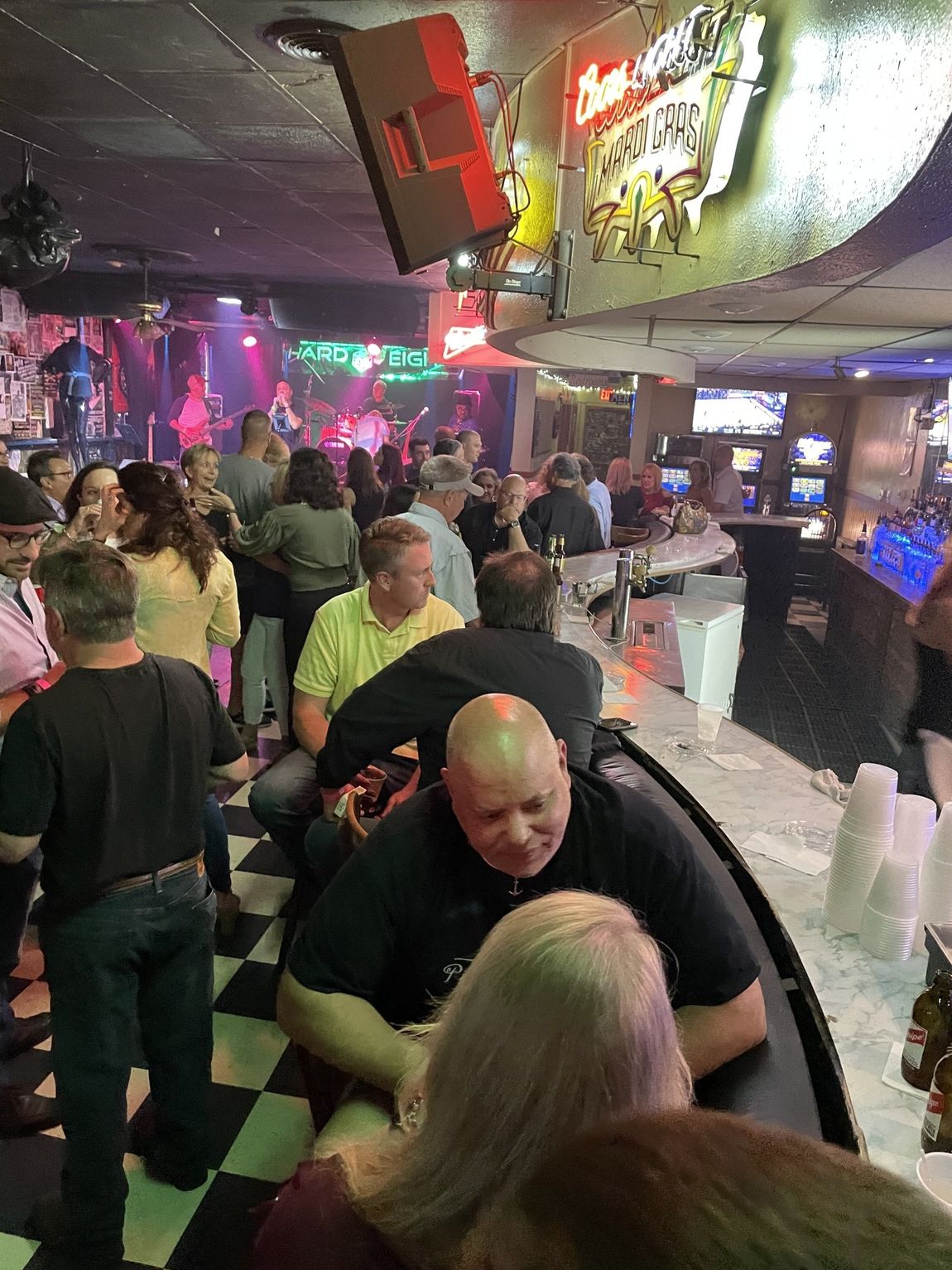 A crowded bar with people at the bar and in front of a stage with a band.