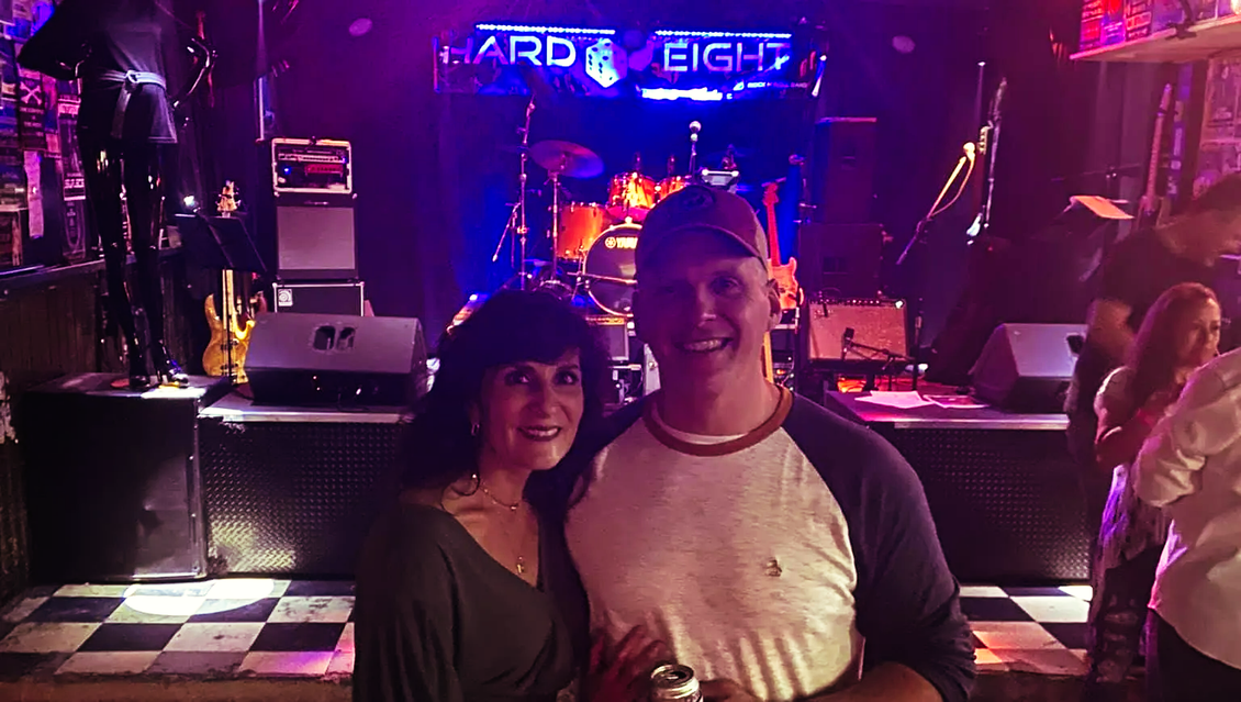 Couple in front of a stage at Hard & Eight bar; stage lit up, instruments visible.