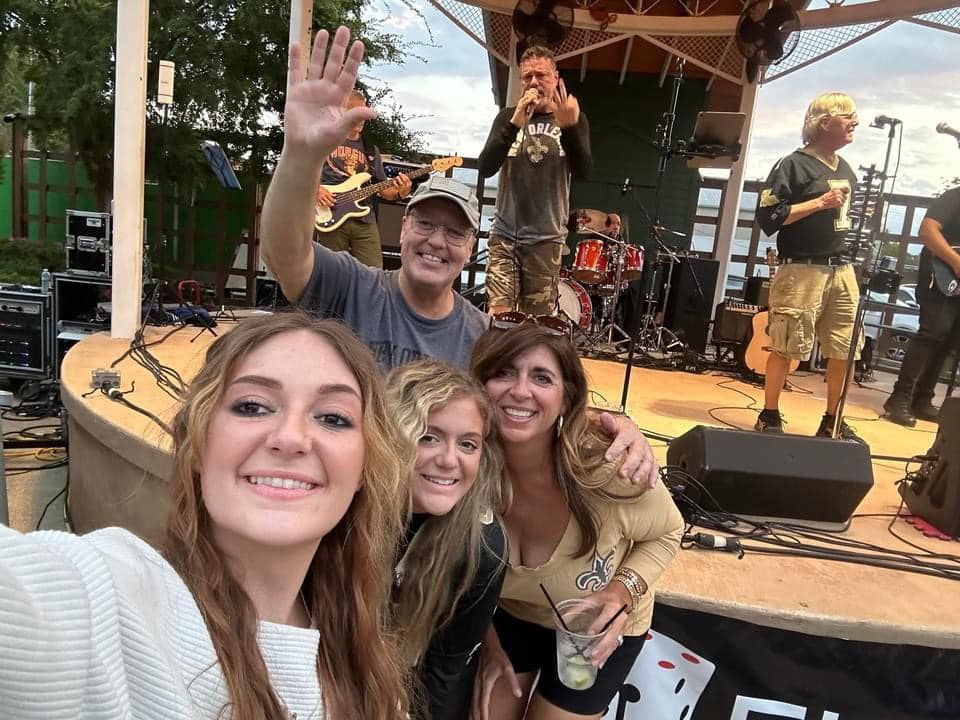 People taking a selfie in front of a band performing on an outdoor stage.