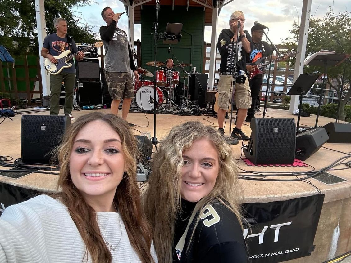 Two women smile in front of a band playing on an outdoor stage.