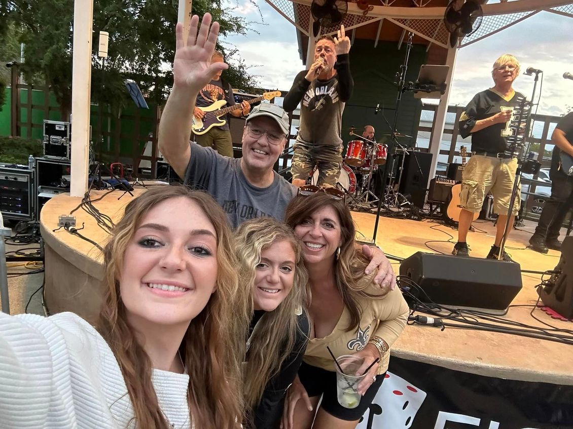 People taking selfie with a band performing on an outdoor stage.