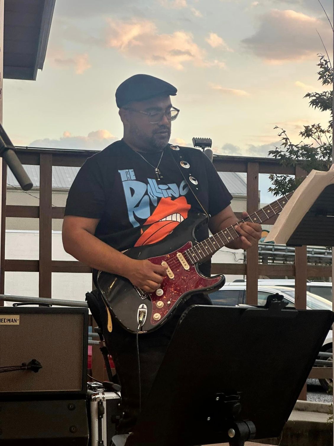 Man playing electric guitar outdoors at dusk.