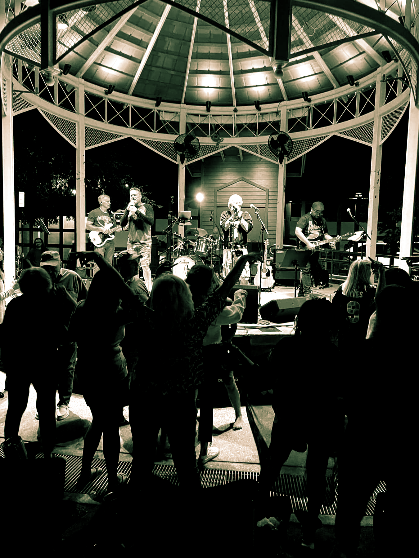 Band performing on a gazebo stage at night; crowd dancing in the foreground.