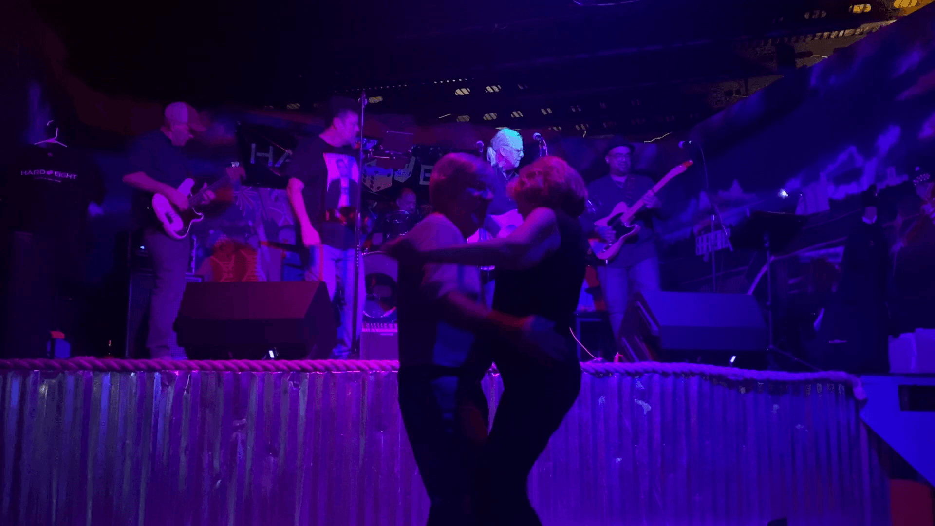 Couple dancing on a stage in front of a band lit with purple lights.