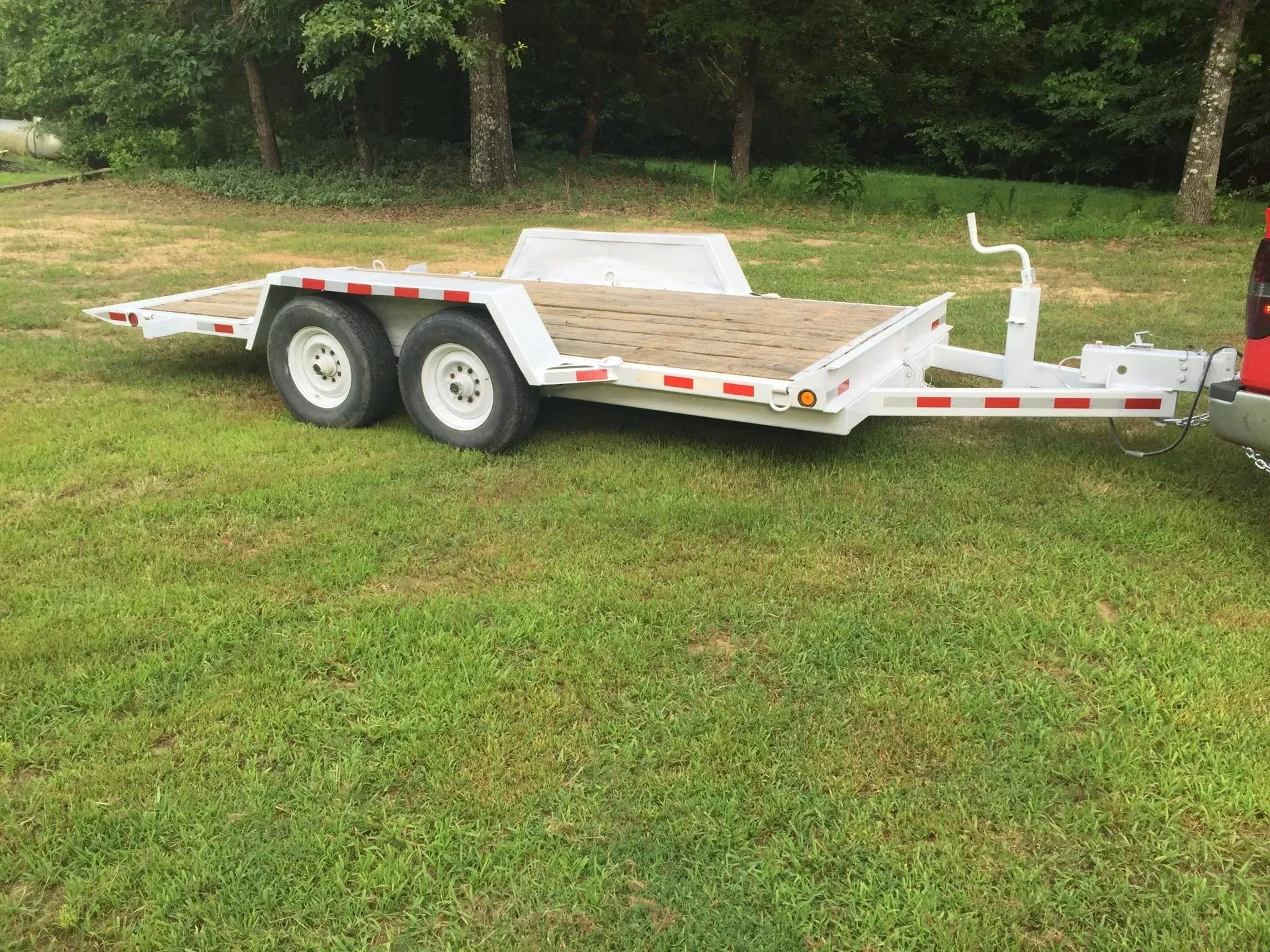 White dual-axle utility trailer parked on grass in a wooded yard