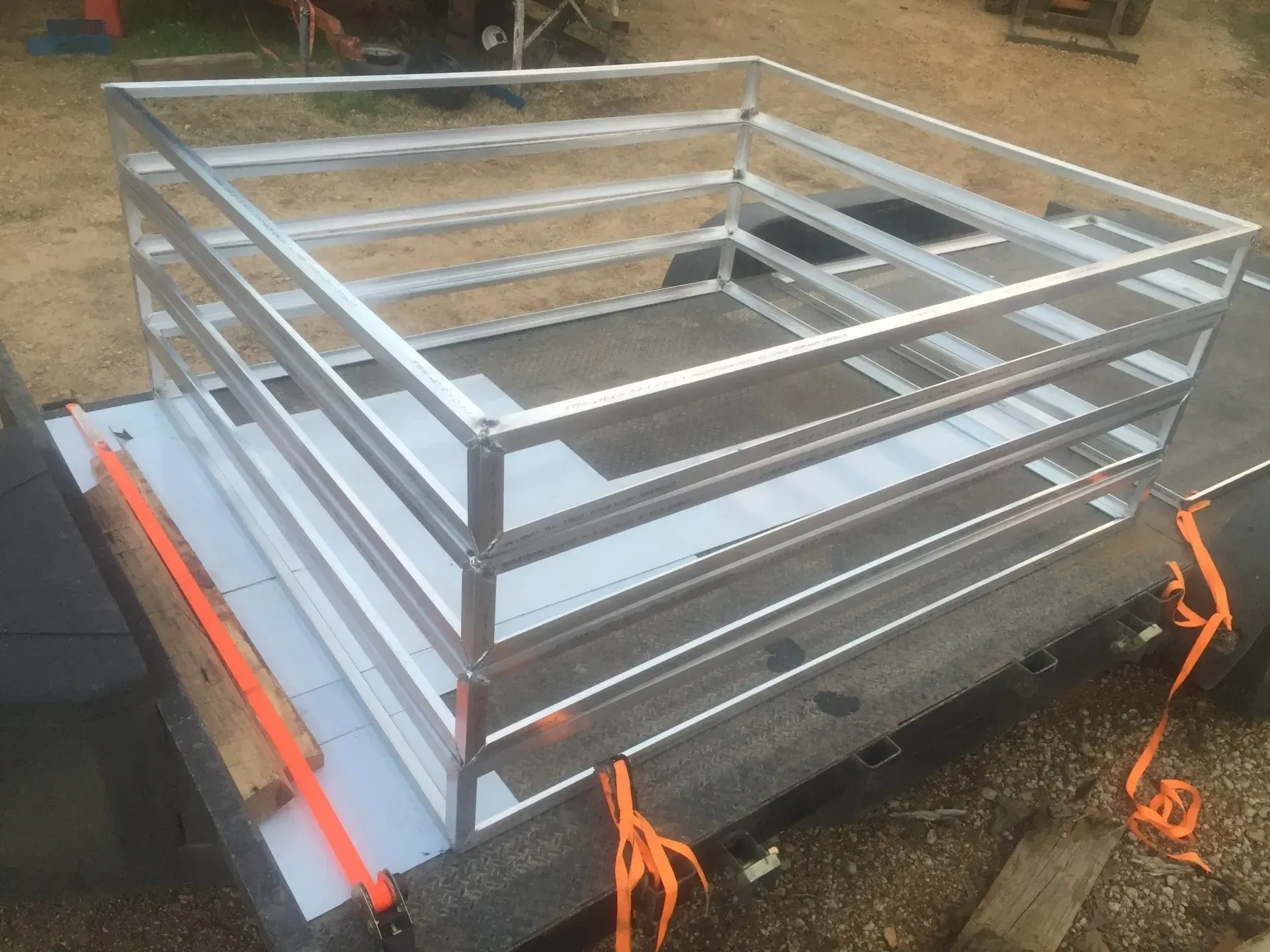Metal cargo rack with silver railings strapped to a trailer bed outdoors