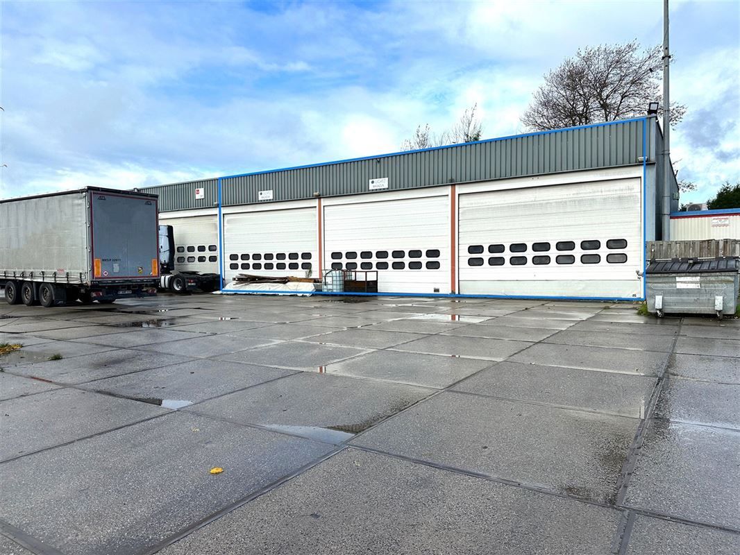 Een gebouw met garagedeuren en een vrachtwagen die buiten op een betonnen ondergrond geparkeerd staat.