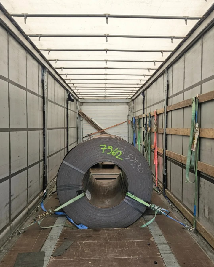 Een grote metalen rol vastgezet in een vrachtwagentrailer met spanbanden en verstevigingen.