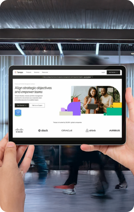Person holding a tablet displaying a webpage with two people on the screen; blurred background.