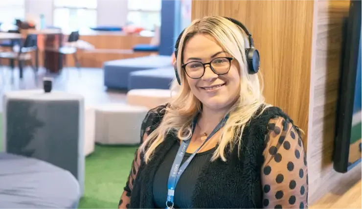 Woman with glasses and headphones smiles at the camera in a modern office.