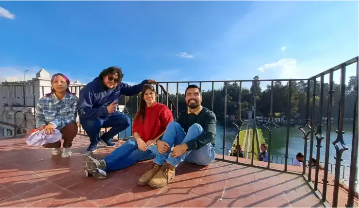Four people sit on a terrace overlooking a lake, posing for a photo under a blue sky.