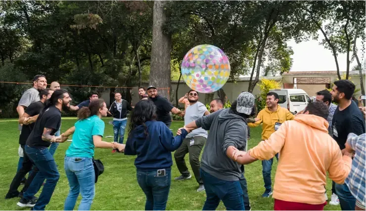 Group of people playing with a large patterned ball in a circle on a grassy field.