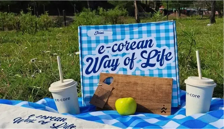 Picnic setting with a blue-and-white checkered box and blanket, two drinks, cutting board, and apple.