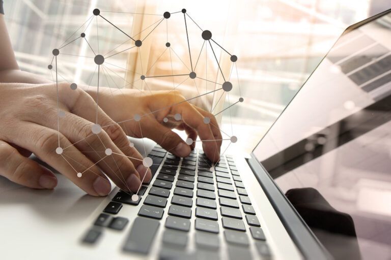 Hands typing on a laptop with an overlaid network of interconnected nodes.