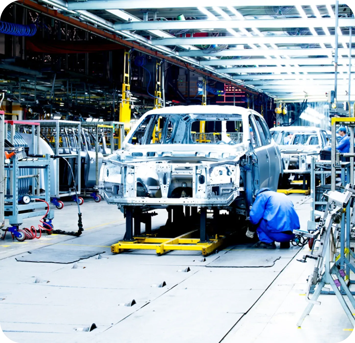 Car assembly line with workers attaching parts to car frames.