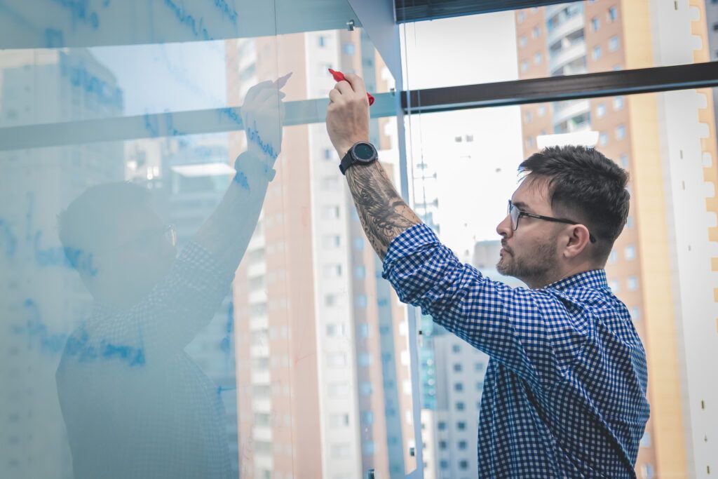 Man writing on a glass wall with a red marker, in a modern office, city view.