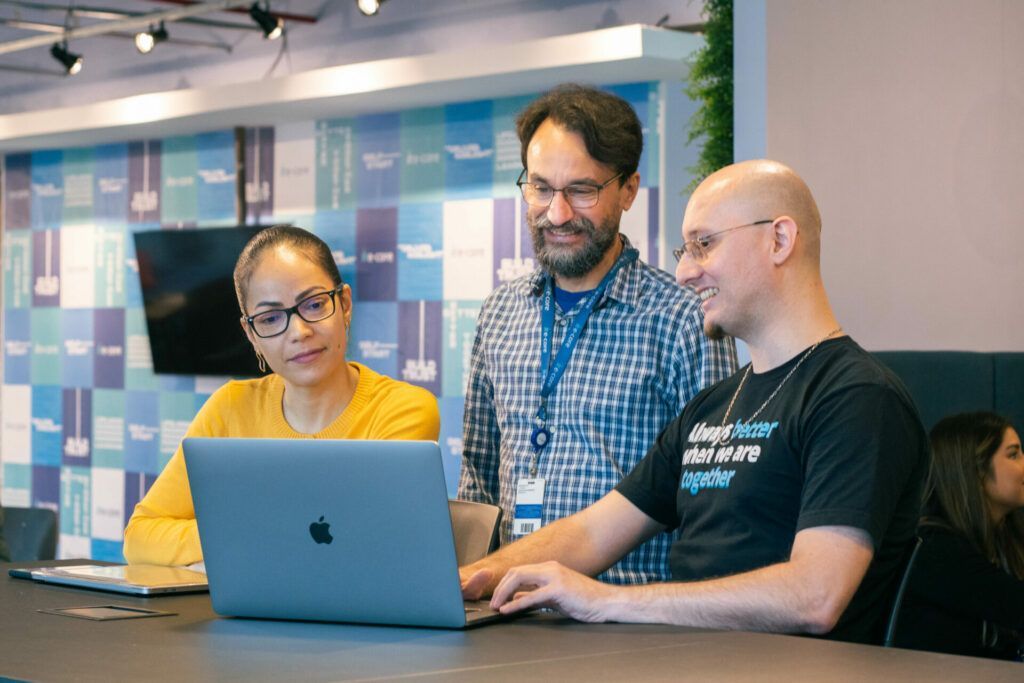 Three people looking at laptop in modern office; teamwork.