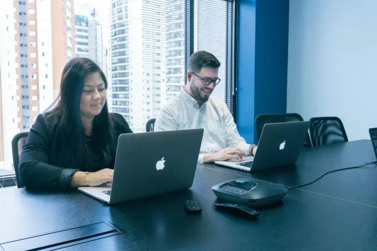 Two people working on laptops at a table in a modern office.