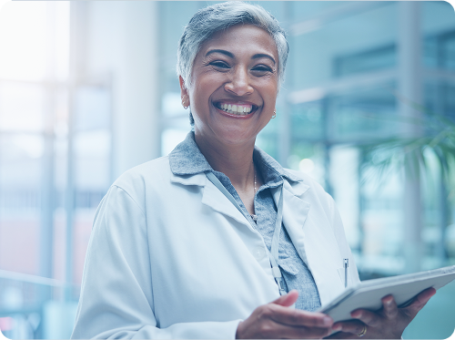 Smiling professional with gray hair in a white coat holding a tablet, indoors.