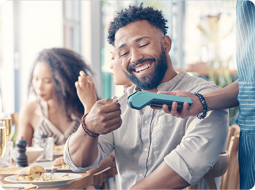 Man smiling while tapping his card on a payment terminal in a restaurant.