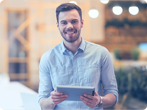 Man holding tablet smiles at the camera in a modern office setting.
