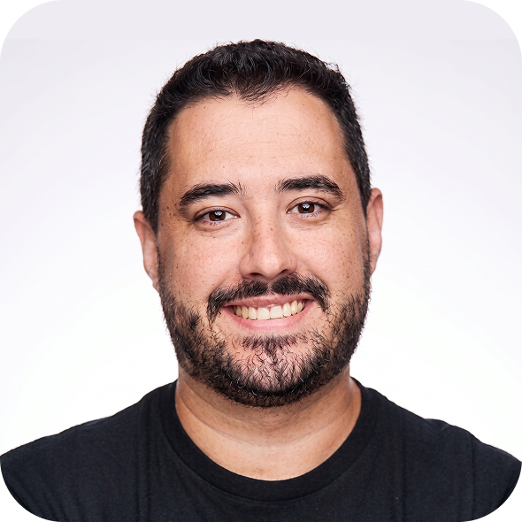 Smiling man with short dark hair and beard wearing a black shirt against a light background