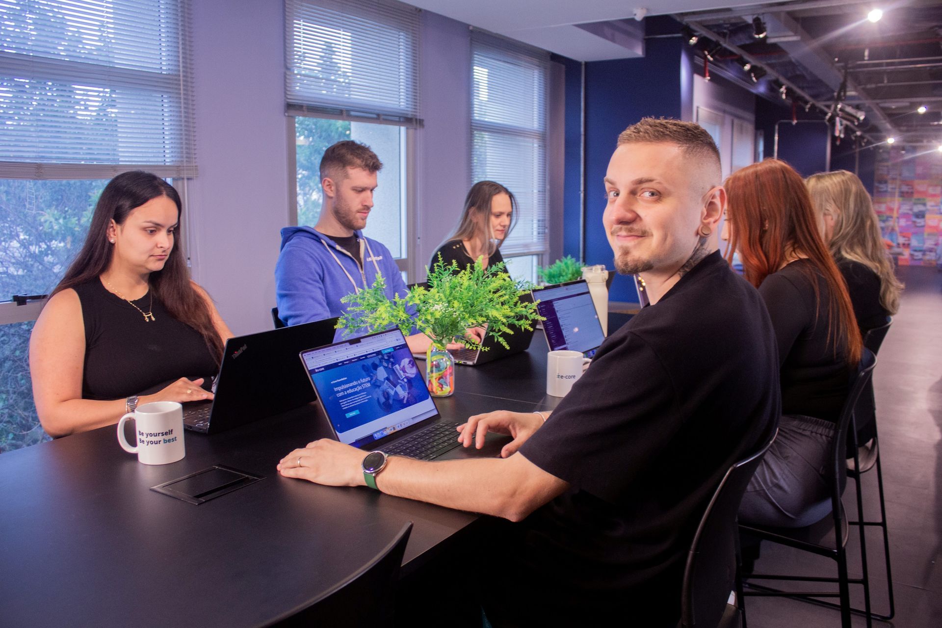 6 people with laptops, working in a table, blue background