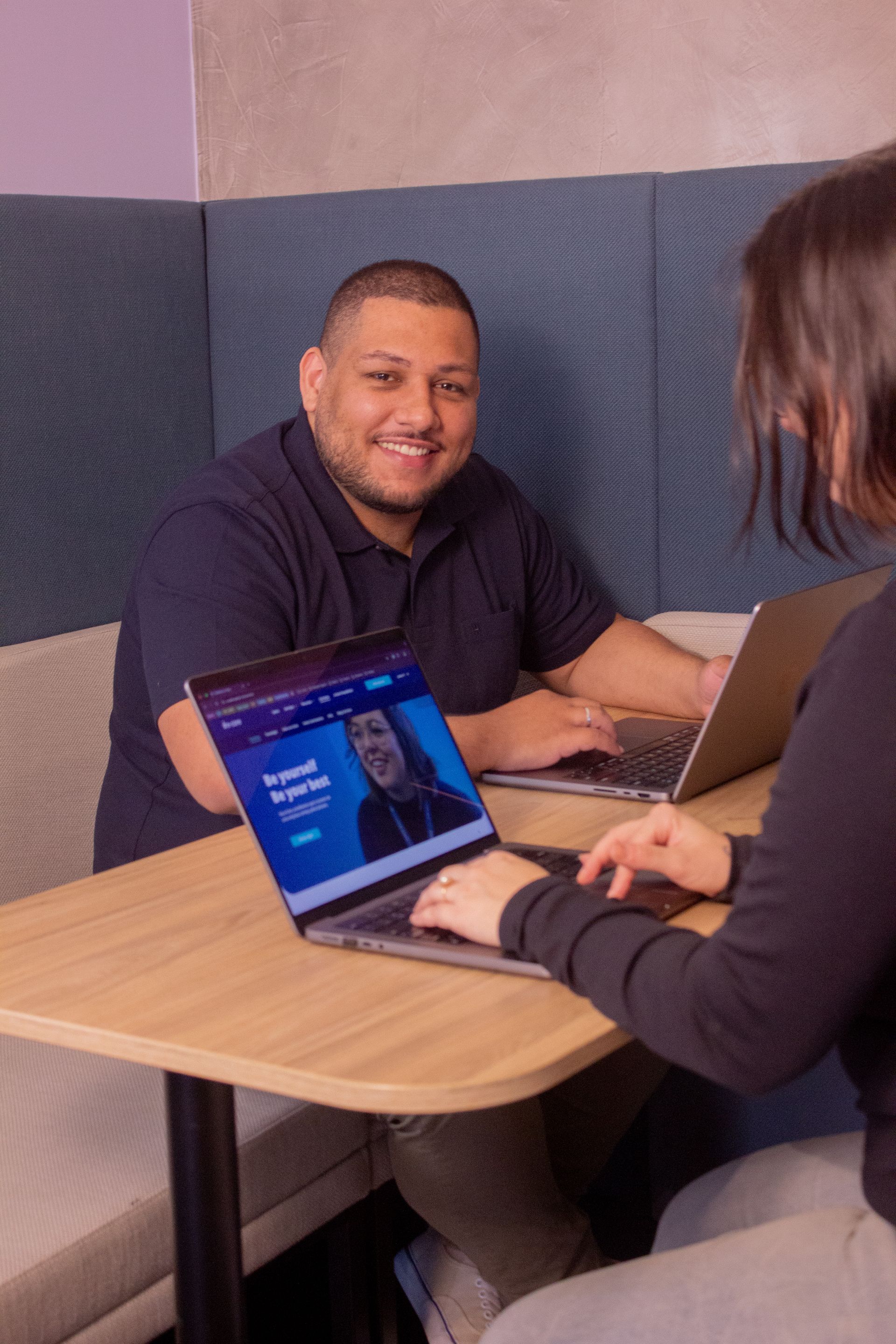 Two people working on laptops at a table in a small booth seating area
