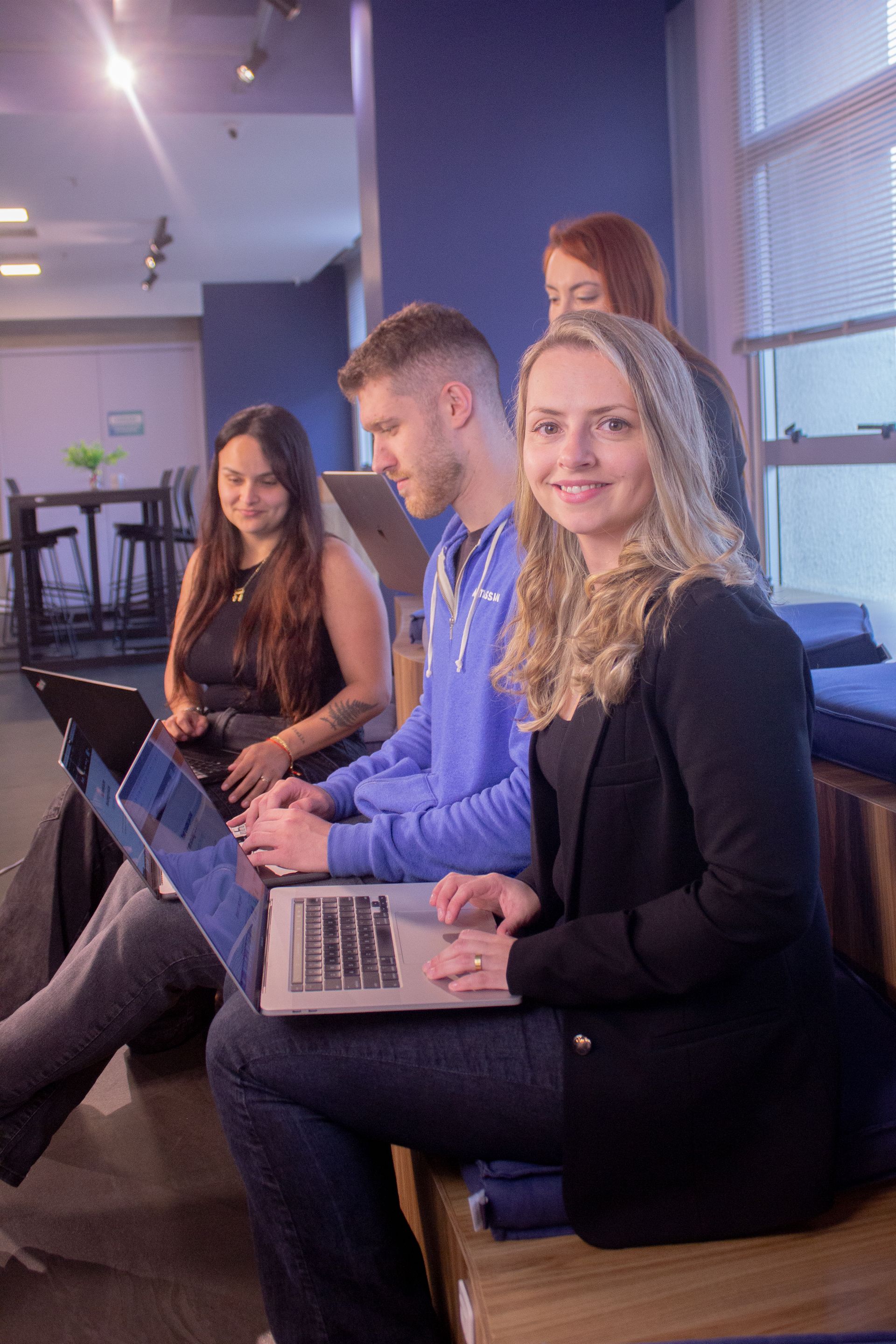 People seated on benches with laptops in a modern indoor lounge, one smiling at the camera.