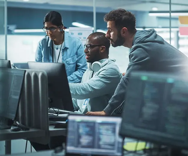 Three people looking at a computer screen in an office setting.