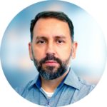 Man with short, dark hair and beard, wearing a blue collared shirt, looking directly at the viewer.