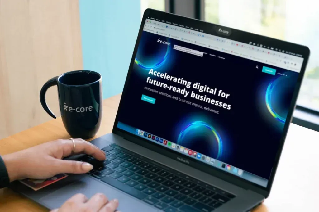 Person using a laptop with a website about accelerating digital businesses. Coffee mug and hand visible.