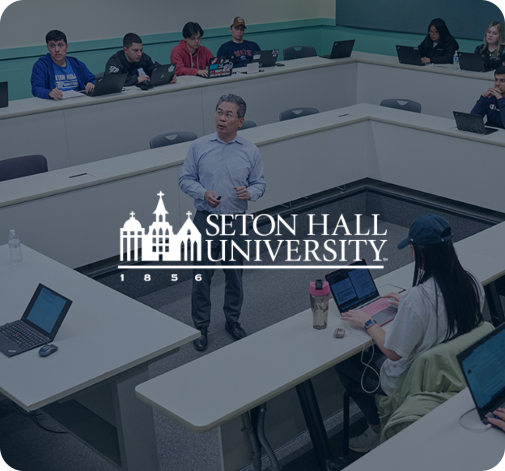 Professor lecturing in classroom at Seton Hall University with students at laptops.