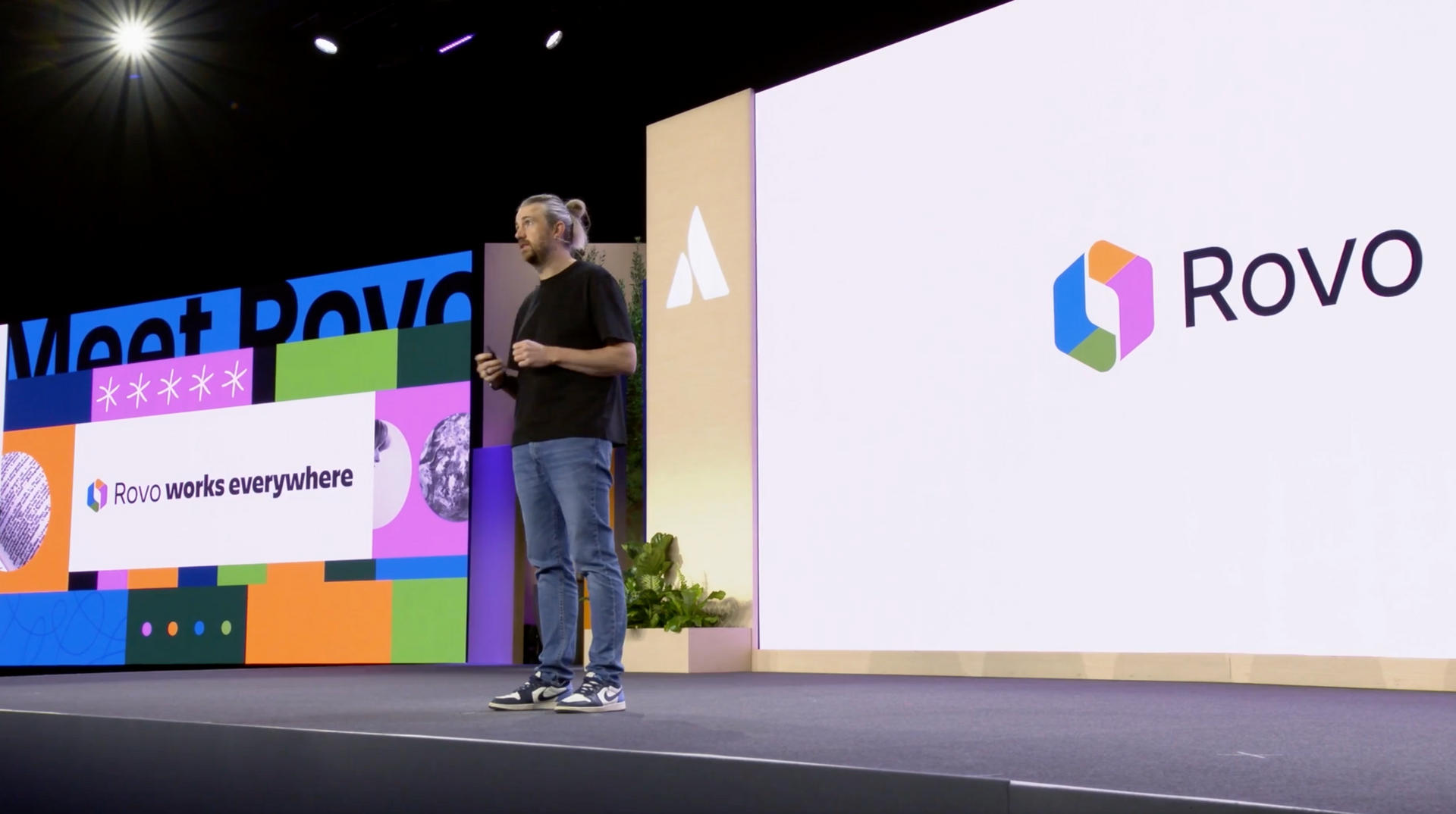 A man presents on stage next to a screen displaying the