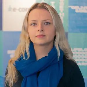 Woman with long blonde hair wearing a blue scarf, looking at the camera.