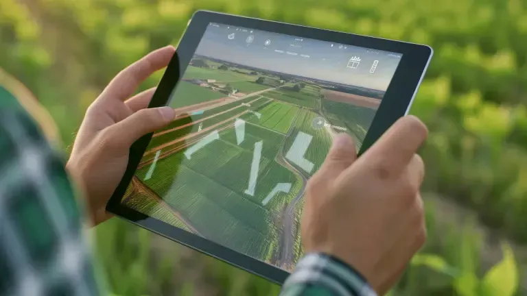 Person holding tablet displaying an aerial view of agricultural fields, outdoors.