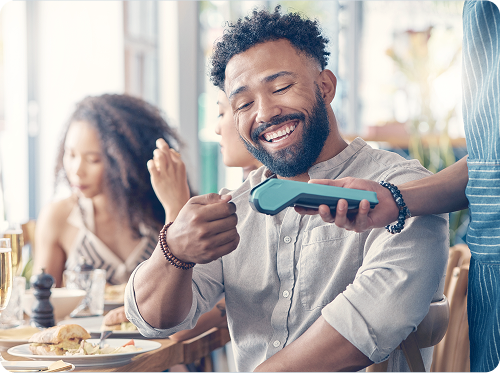 Man smiling while paying with contactless card reader at a restaurant.