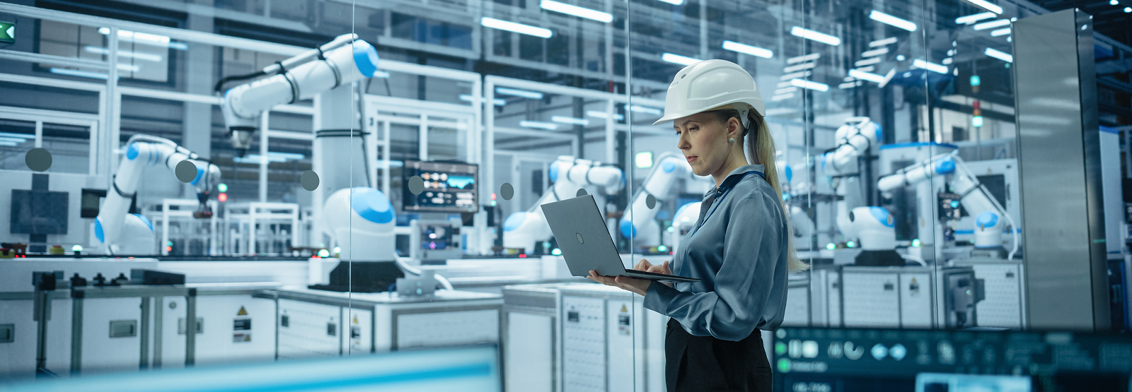 Factory worker monitoring robotic arms on an automated assembly line.