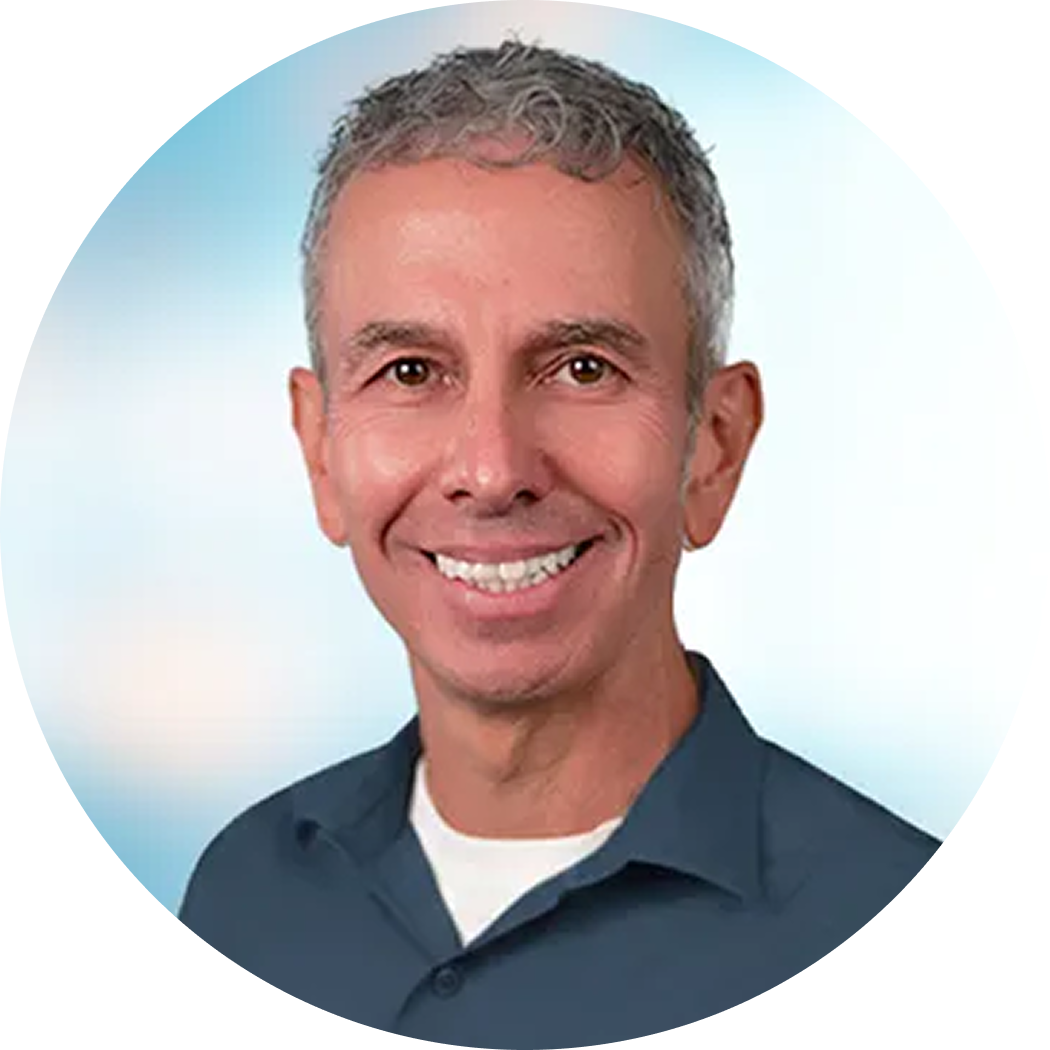 Smiling man with short gray hair in a dark blue shirt against a light blue circular background