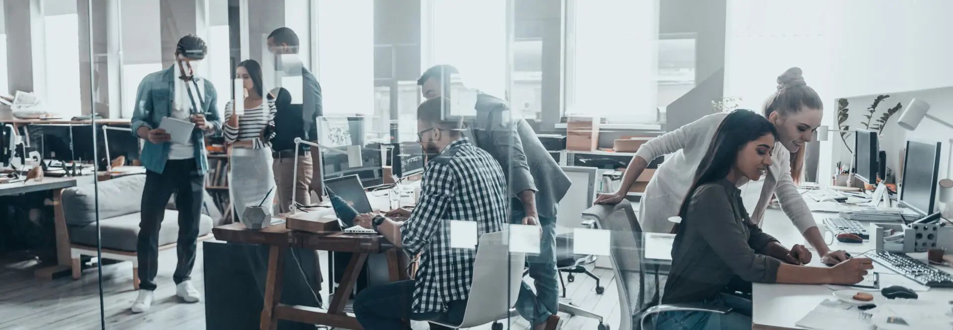 People working in a modern office, behind a glass wall. Some are wearing face masks.