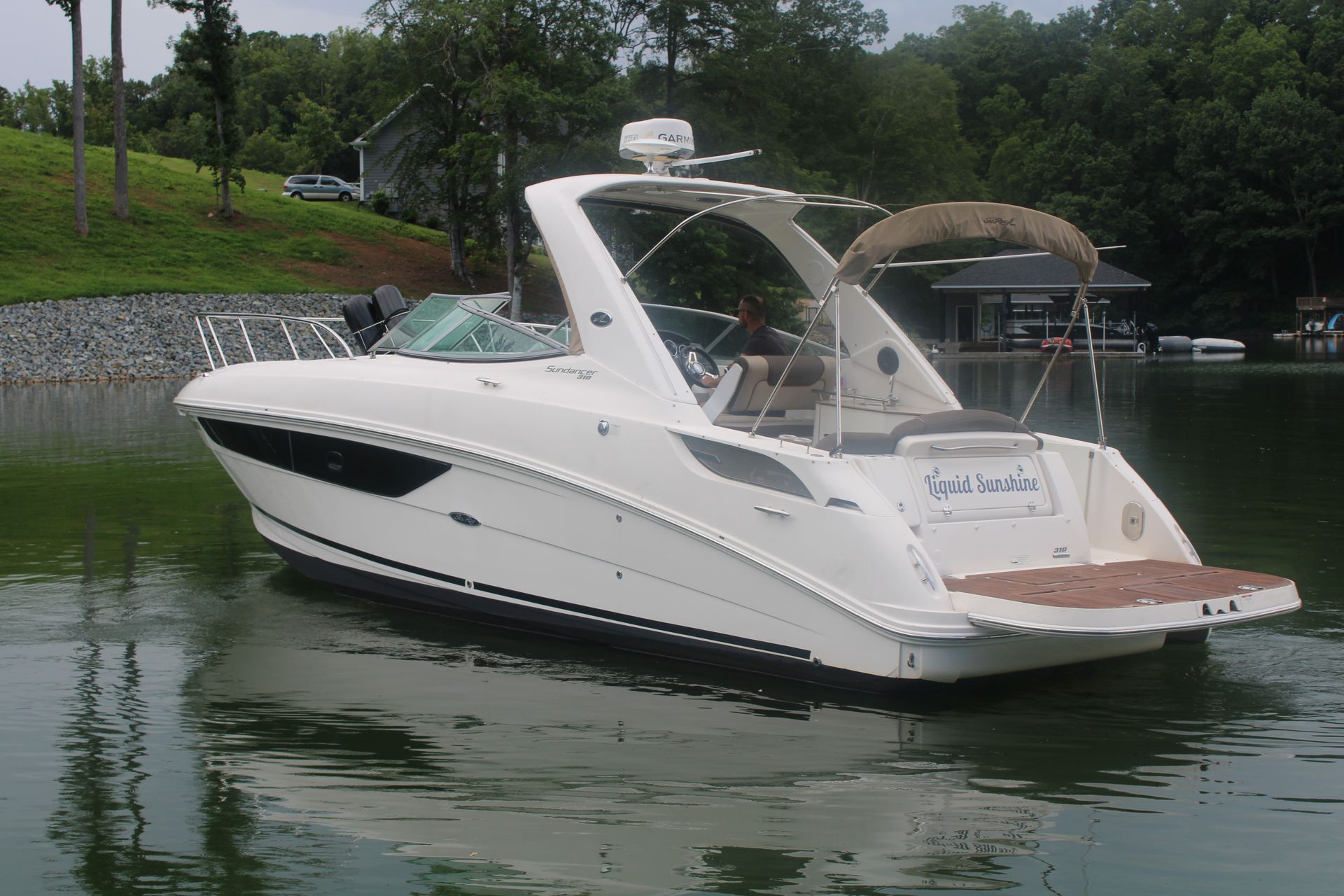 White motorboat on calm water near a shoreline with trees and a building in the background.
