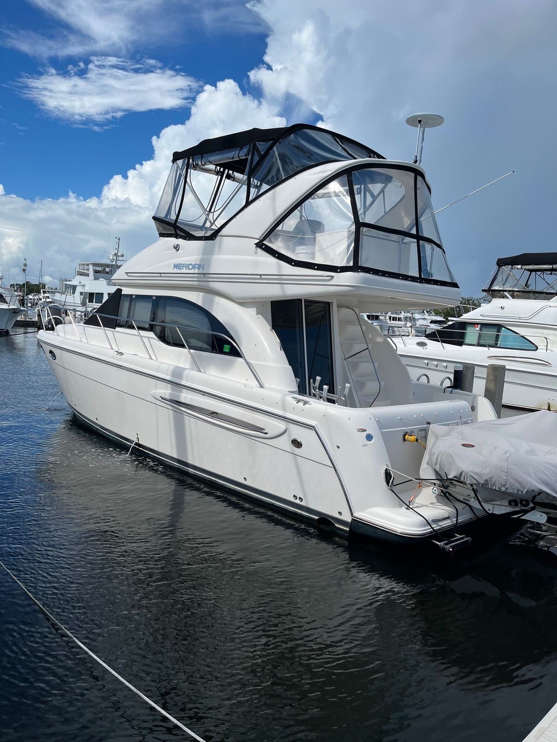 White yacht docked at a marina on a sunny day with blue sky and white clouds.