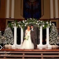 Bride and groom standing on a decorated church altar with white flowers and candles